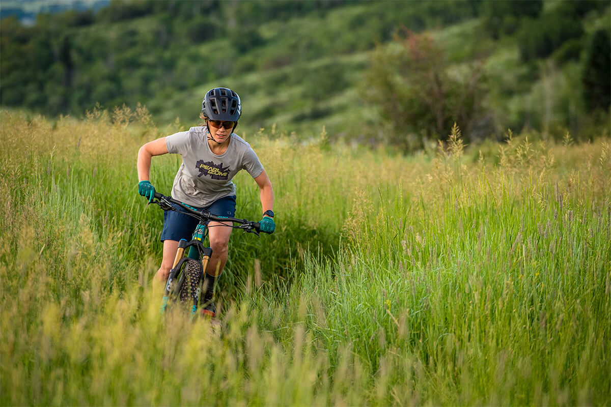 Women mountain biker riding through grass field wearing a Lazer Impala MIPS helmet