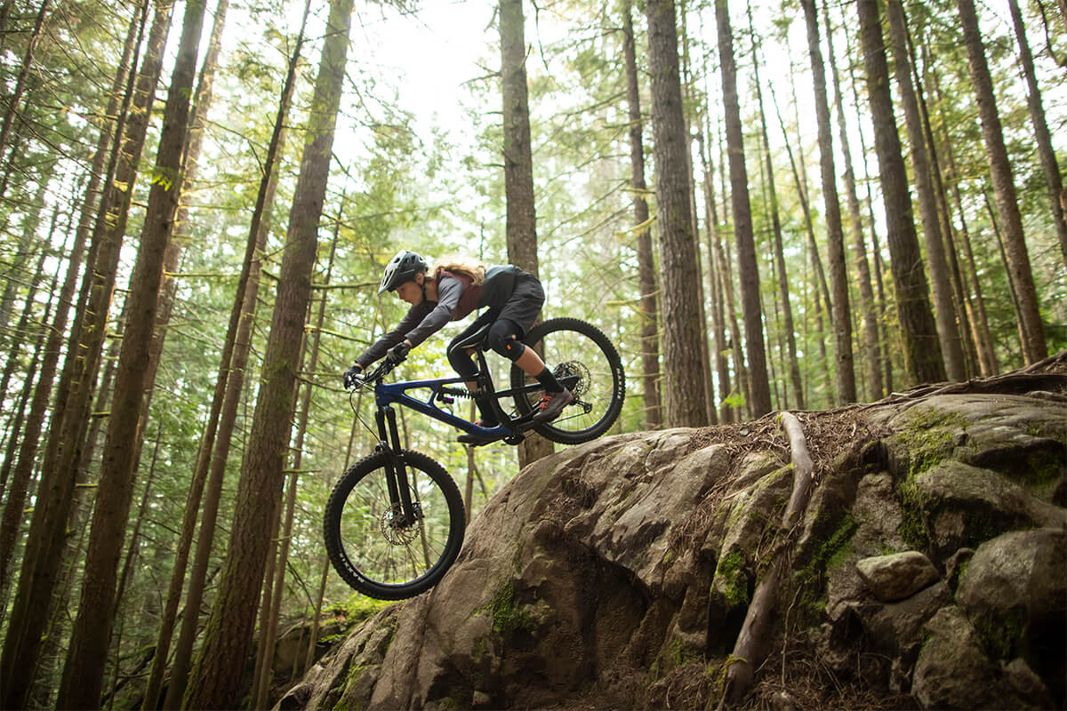 Female Mountain biker riding down large rock wearing a Lazer MIPS helmet. Learn how MIPS provide better protection 