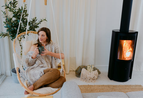 Genna sits on a hanging chair by the fire with a cup of tea looking pensively out the window