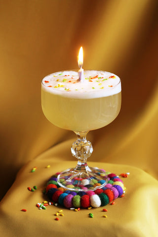 Cocktail in a coupe glass with a lit candle in the middle, egg white foam and candied fennel sprinkles