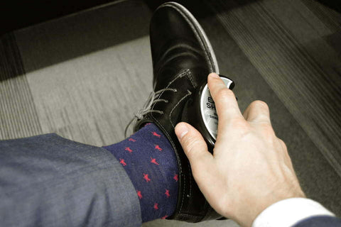 Homme avec chaussettes fantaisie en train de cirer ses chaussures en cuir noir.