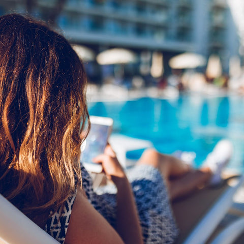 woman sitting by hotel pool using her phone