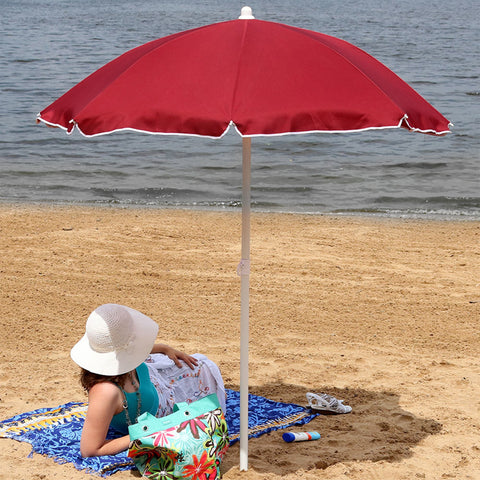 Woman laying on the sand at the beach with an umbrella shading her