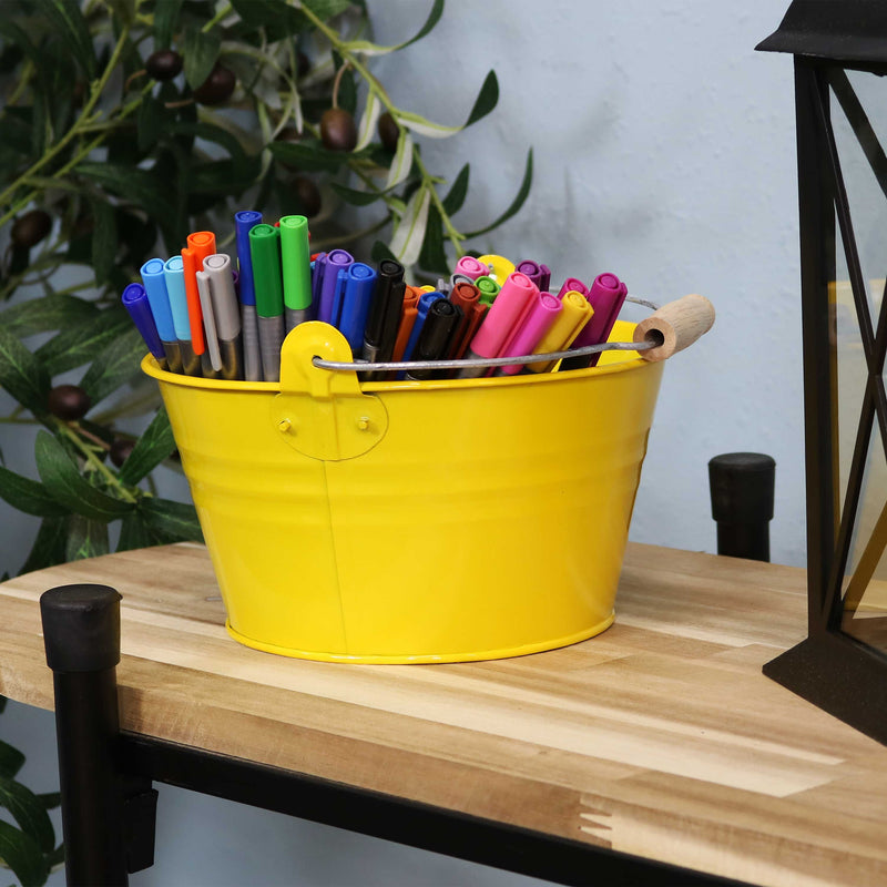 Four yellow galvanized steel buckets with handle filled with various items placed bookshelf containing books and pictures.
