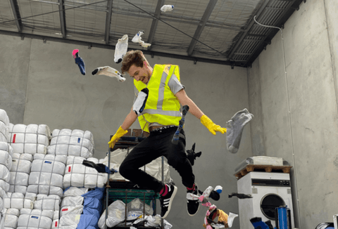 man in a working vest jumping and clothes all around him, to illustrate the need for businesses that give back in Australia and use recycling and sustainable methods