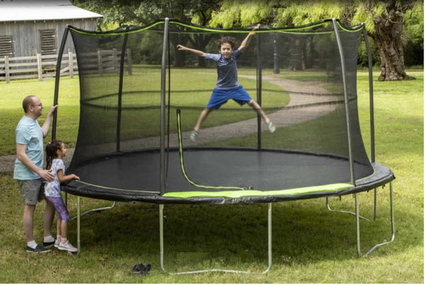 A kid jumping on a 14 ft trampoline while his family watches.