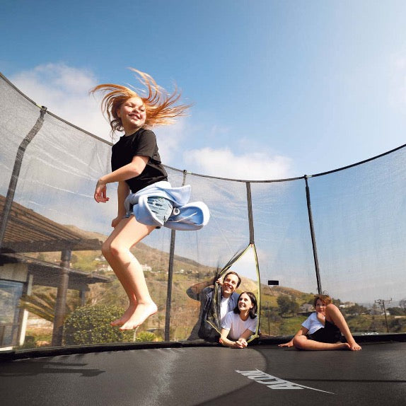 A girl doing a twist on an ACON Trampoline while her family watches from the zipper door.