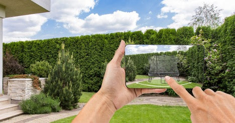 A person holding a smartphone in a backyard with a Springfree Trampoline on the screen.