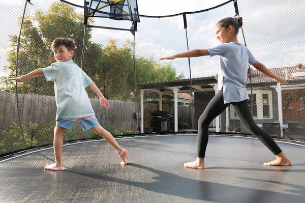 Two kids doing yoga poses on a trampoline.