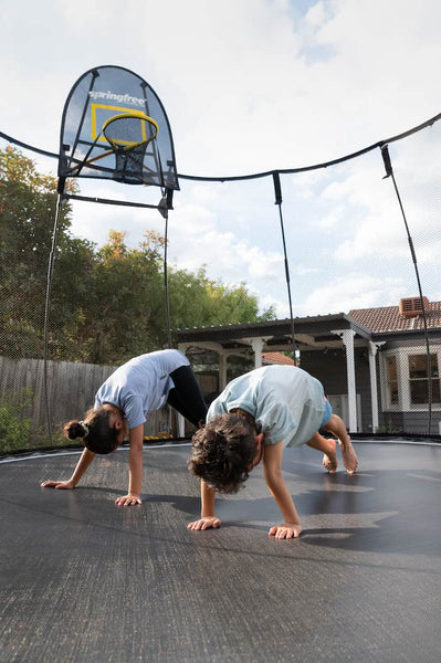 Two children doing the downward dog move on a trampoline mat.