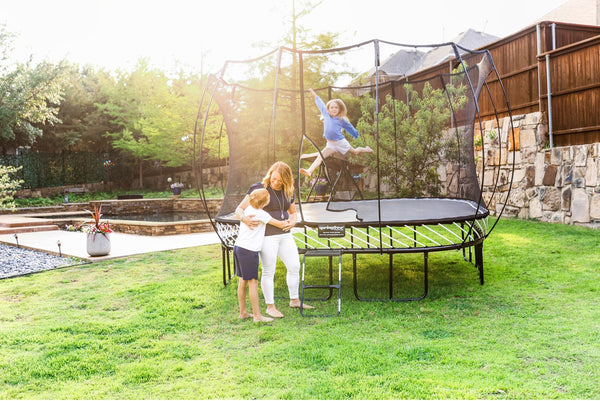 A mom hugging her son while her daughter jumps on a Springfree Trampoline.