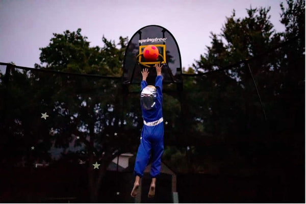 A child dunking on a trampoline basketball hoop with an astronaut suit on.