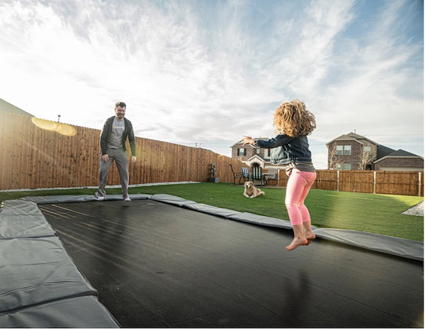 A father and daughter jumping simultaneously on an inground trampoline.