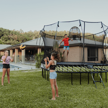 A kid jumping on a Springfree Trampoline while two other kids throw a ball outside of it.
