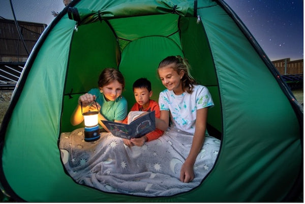 Three kids reading a book in a green tent.