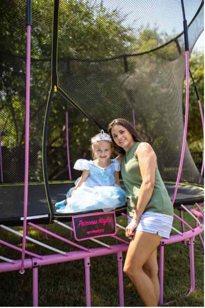 A mother and daughter smiling next to a pink Springfree Trampoline.