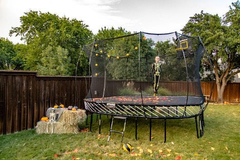 A kid in a Halloween costume jumping on a Springfree Trampoline with fake leaves on it.