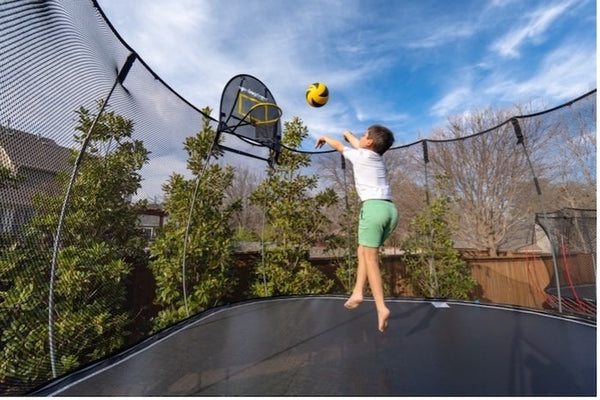 A boy shooting a basketball on a trampoline basketball hoop.