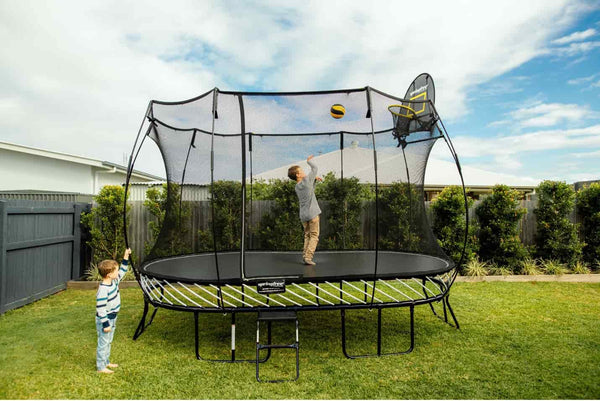 A kid shooting baskets on the Springfree Basketball Hoop while another kid stands and watches from the outside.