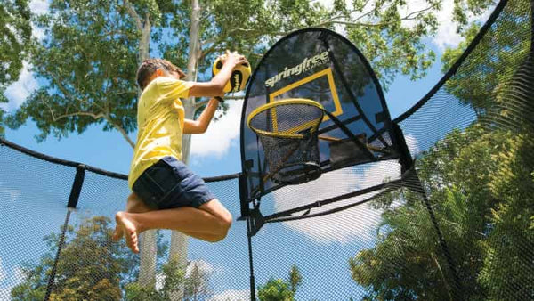 A boy dunking on a Springfree Trampoline Basketball Hoop.