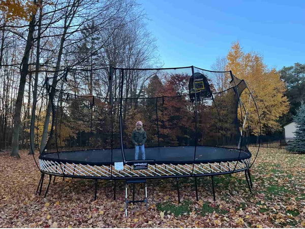 A kid dressed in winter clothes standing on a Springfree Oval Trampoline.
