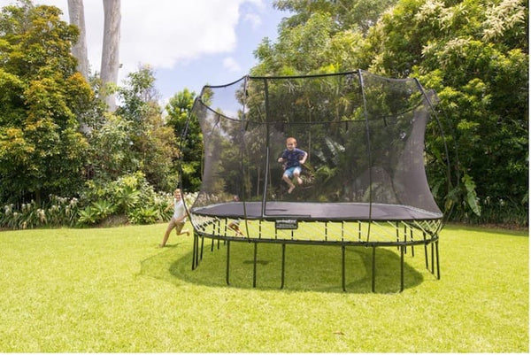 A little boy jumping on a Springfree Trampoline while another kid runs around it.