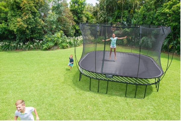 A girl jumping on a Springfree Trampoline while two kids run around it.