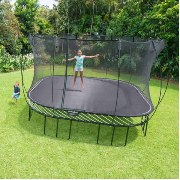 A girl jumping on a Springfree Square Trampoline while a boy runs around it.