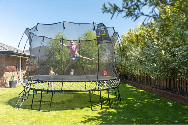 A smiling girl jumping in mid-air on a Springfree Trampoline.