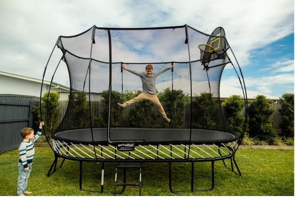 A boy jumping on a Springfree Trampoline while his brother watches from the outside.