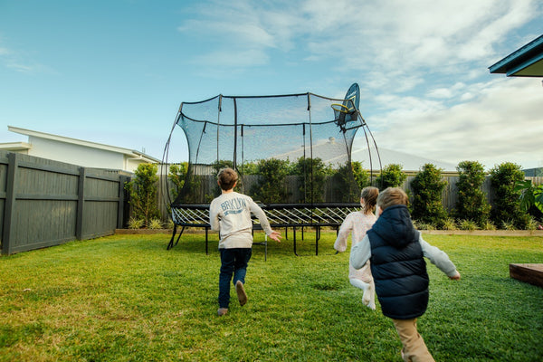 Three kids running to their Springfree Large Oval Trampoline.