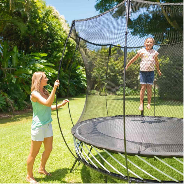 A mother watching her young daughter as she jumps on a Springfree Trampoline.