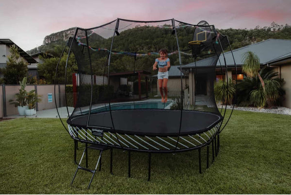 A girl jumping on a Springfree Trampoline with lights around it in the evening.