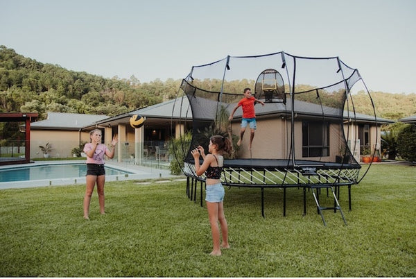 Two girls throwing a ball next to a boy jumping on a Springfree Trampoline.