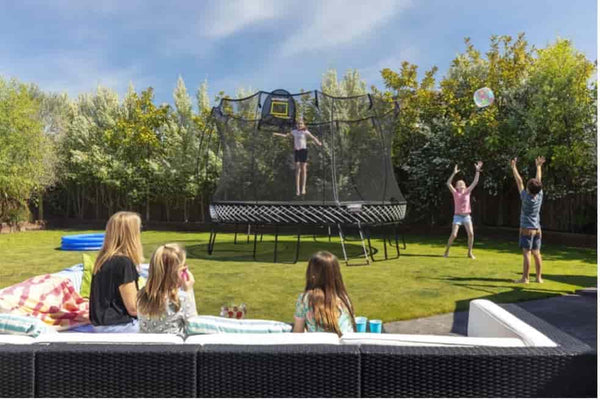 A child jumping on a Springfree Trampoline in a backyard with multiple people around.