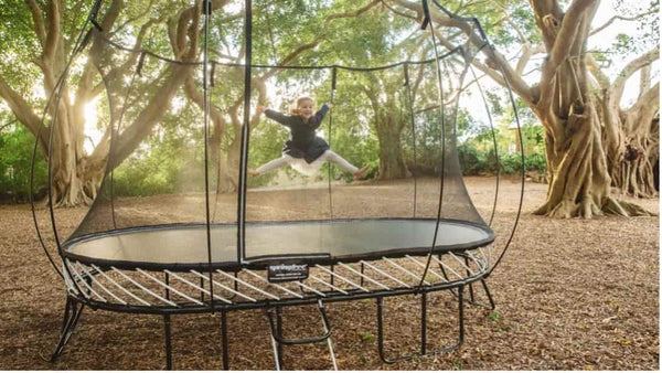 A little girl jumping on a Springfree Trampoline in a shaded area.