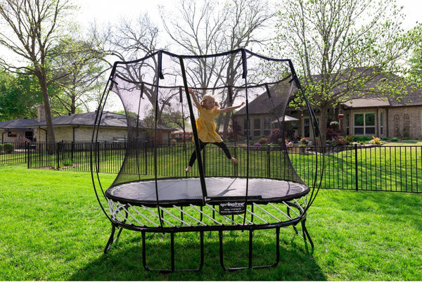 A girl in a yellow shirt jumping on a Springfree Trampoline.