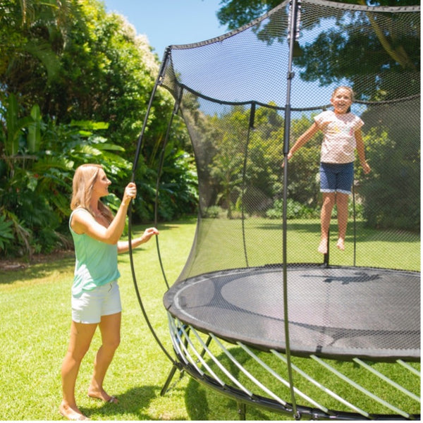 A little girl jumping on a Springfree Trampoline while her mom watches.