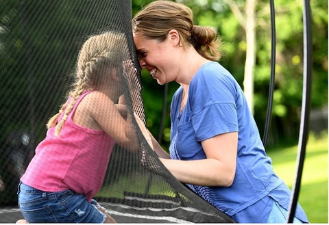 A mother looking at her daughter through a trampoline net, smiling.