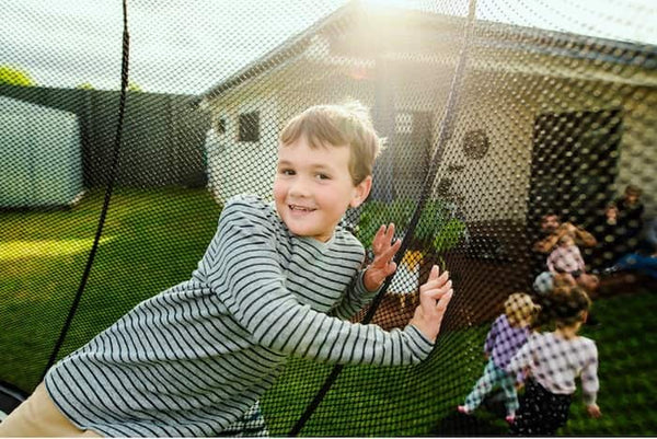 A boy leaning against the Springfree Trampoline net.