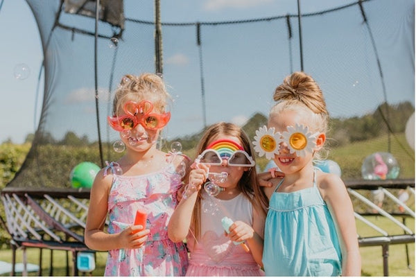 Three girls with colorful glasses and bubbles by a Springfree Trampoline.