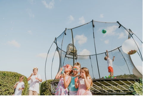 Kids blowing bubbles at a party with a Springfree Trampoline.