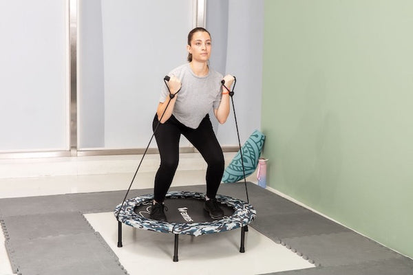 A woman using resistance bands on a rebounder trampoline.