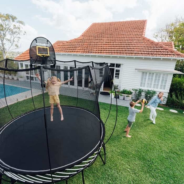 A little girl jumping on a round trampoline while a mom and son throw a ball nearby.