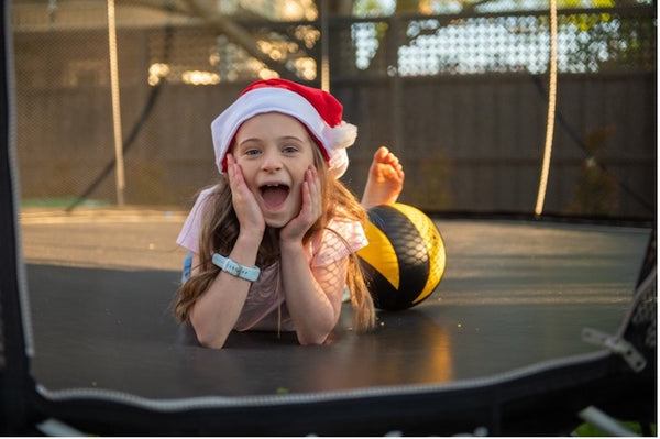 A girl in a Santa hat smiling big while laying on a Springfree Trampoline.