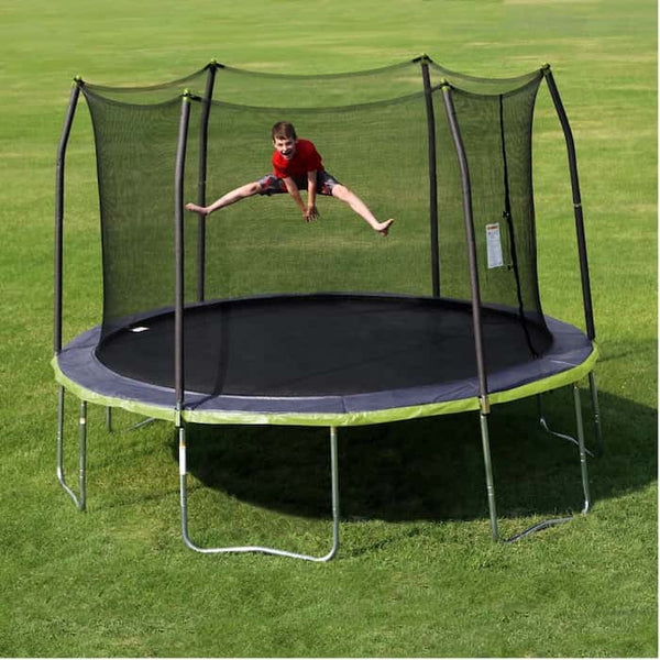 A boy doing the splits in mid-air on a green and black trampoline.