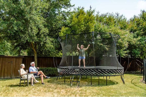 An older kid jumping on a Springfree Trampoline while her grandparents watch.