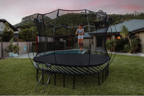 A girl jumping on a Springfree Trampoline with lights around it in the evening time.