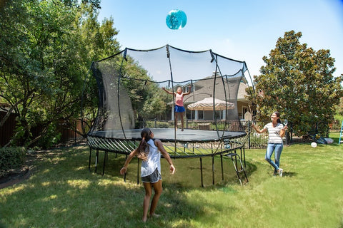 A little girl getting ready to catch a ball on a Springfree Trampoline with her mom and sister watching.