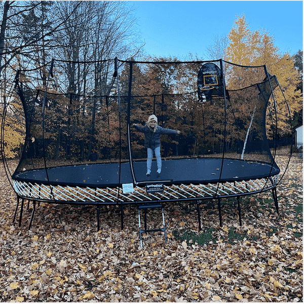 A child dressed in warm apparel smiling on a Springfree Trampoline.